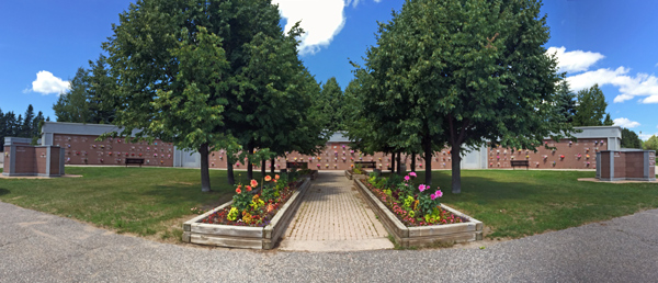 View of a brick mausoleum surrounded by lush trees and vibrant flowers in a scenic outdoor setting.