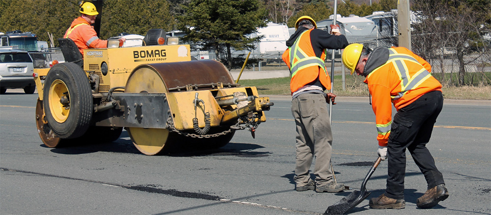 A group of workers is actively repairing a road, using tools and equipment under a clear sky.