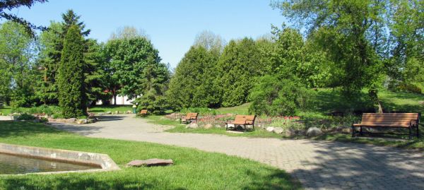A vibrant green park path with flower beds and commemorative benches