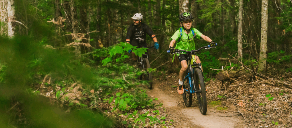 A child and an adult ride through a bike trail through the forest at Hiawatha