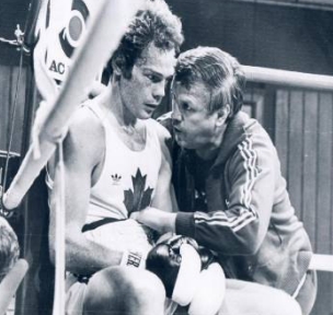 Kenny Casola sitting down in the ring while his coach gives him a talk